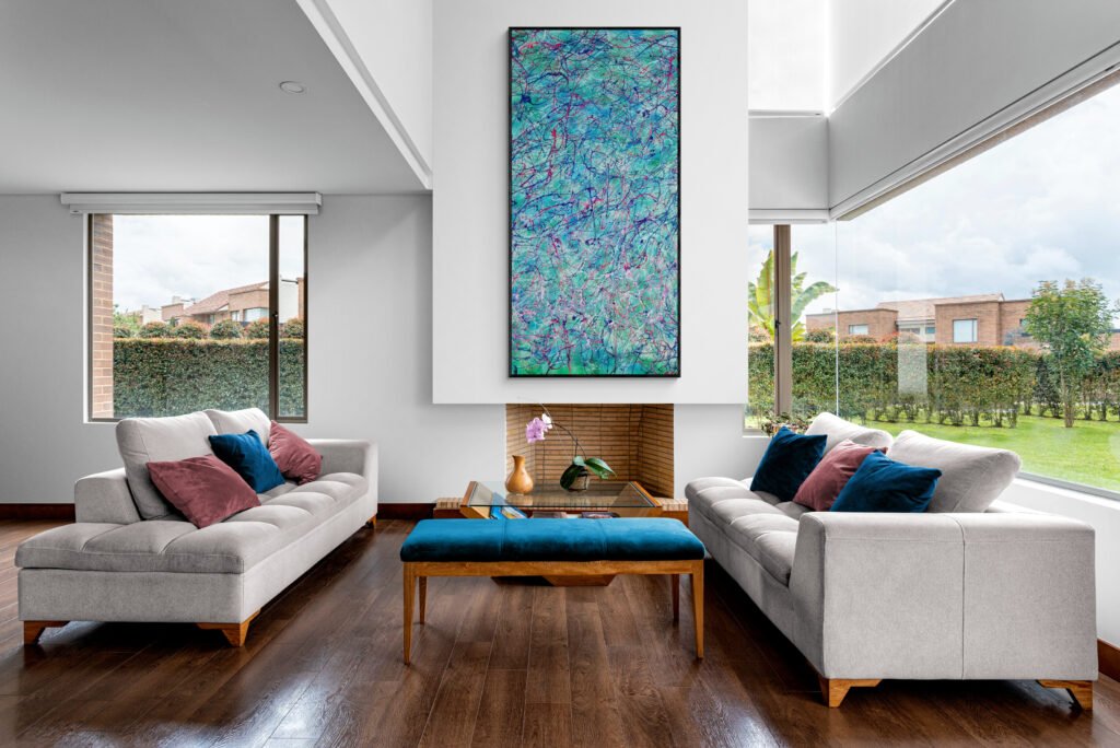 Vibrant tropical-style abstract art as the focal point above a modern fireplace in a bright living room with large windows and garden views