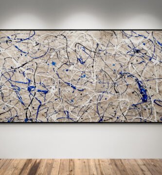 Jackson Pollock style sand, blue, and white abstract canvas art displayed in a modern gallery space with wooden floors and spotlights.