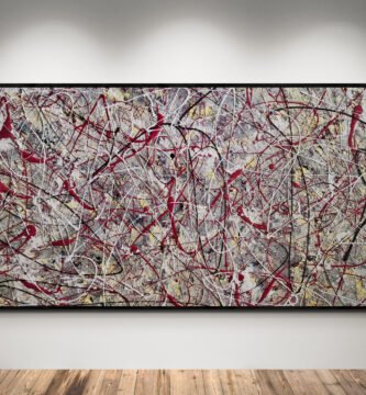 Jackson Pollock style abstract canvas in wine red, gray, yellow, and white tones, displayed in a modern gallery with wooden flooring.